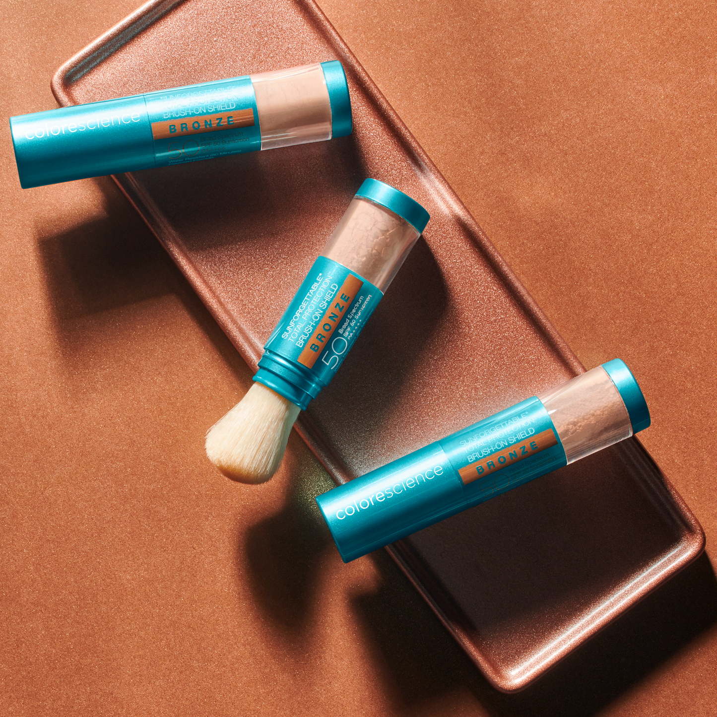 Lifestyle product image of three sunforgettable brush on spf bronzers on bronze plate