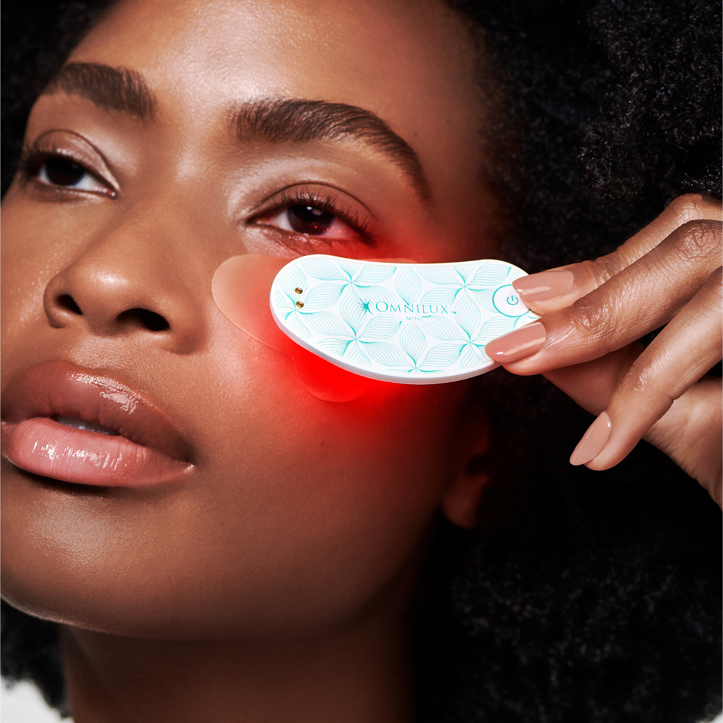 Youthful woman using omnilux infrared device on undereye area with patch