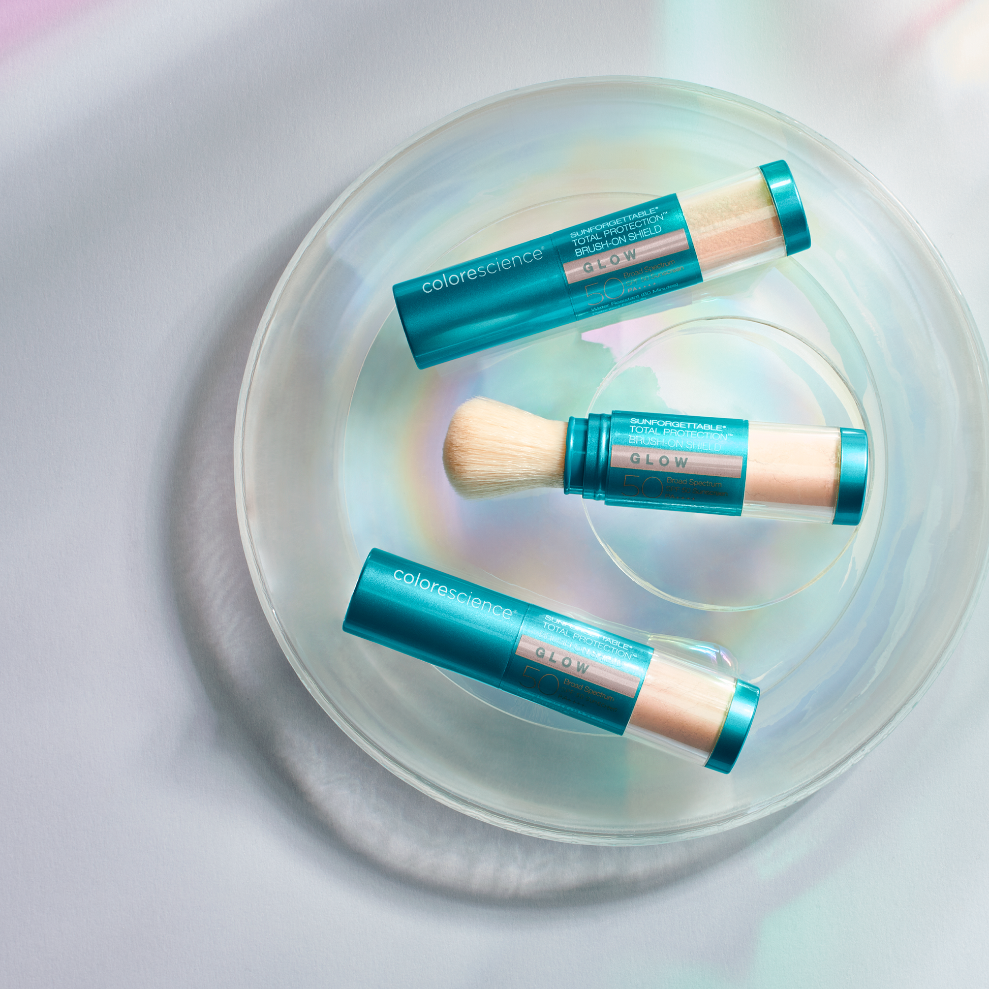 Lifestyle image of three colorescience brush on shield glow spf cases on clear plate